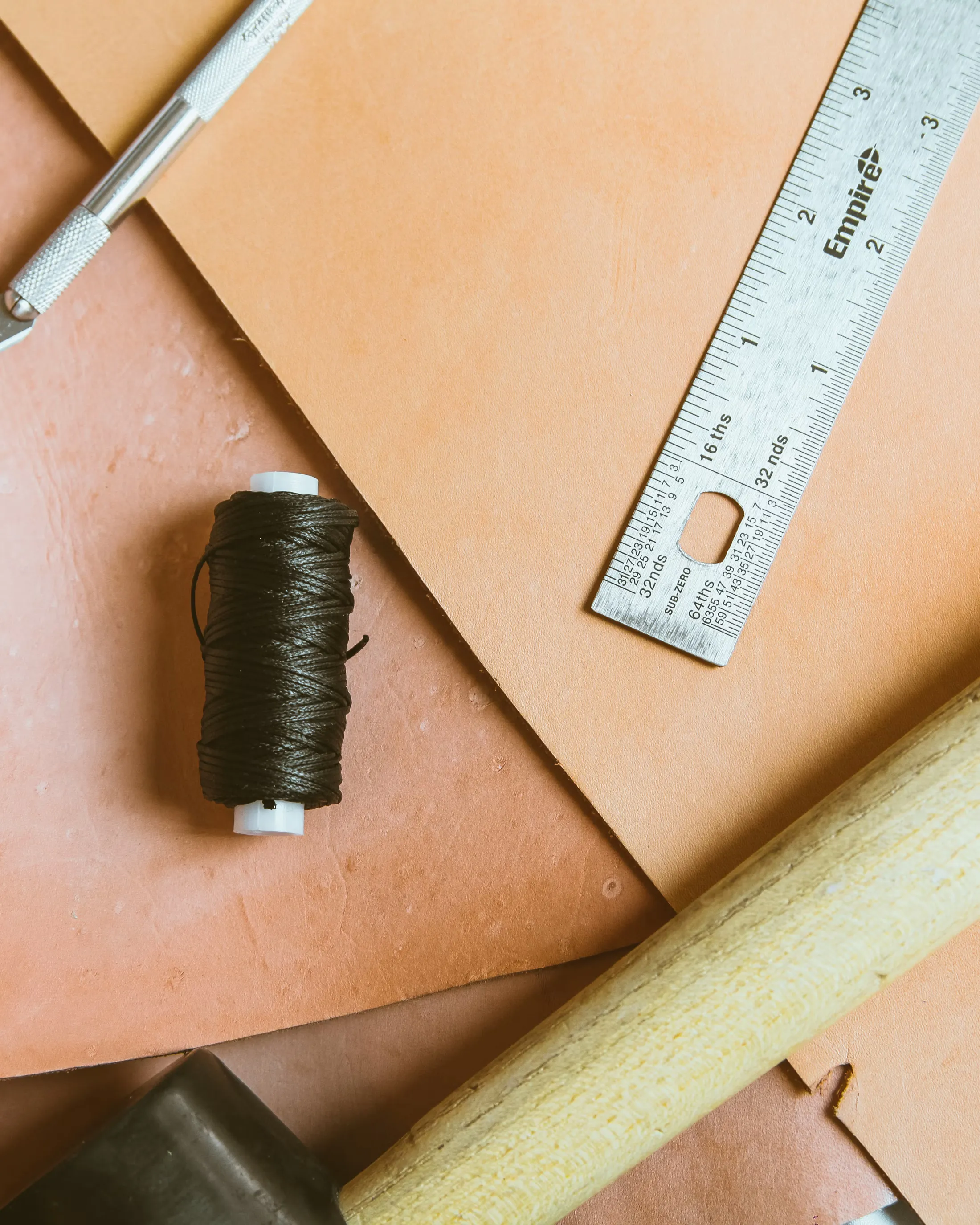 Leather cutting tools: hide, ruler, waxed thread, and knife on a workbench